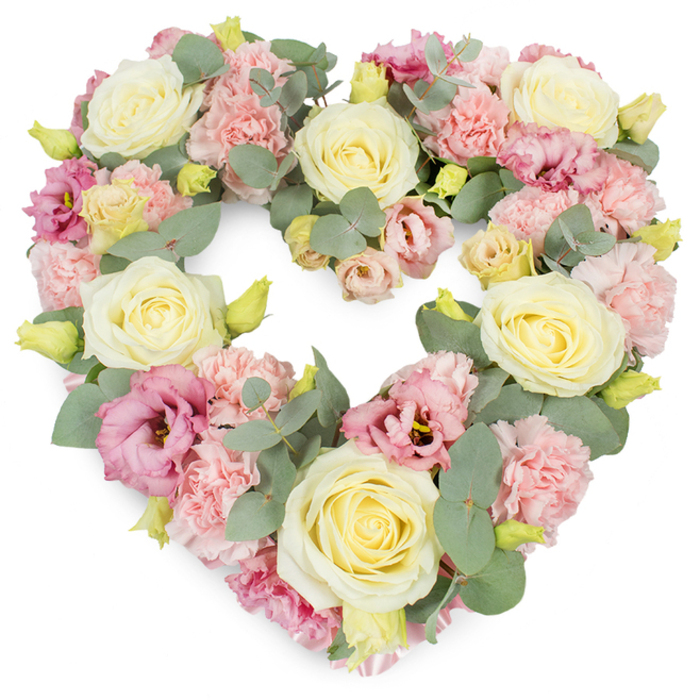 A beautifully detailed, heart-shaped floral tribute dominates the scene, set against a crisp white background that showcases every nuance of colour and texture, the kind of handcrafted piece you might find created with care in an Honor Oak flower studio. The heart is full and symmetrical, defined entirely by flowers and foliage with no visible frame, giving it a soft but well-structured presence. Large, creamy ivory and pale yellow roses are positioned throughout the design, their petals tightly swirled in the center and gently opening at the edges, lending a sense of elegance, purity, and enduring affection. Between and around these roses, clusters of light pink carnations add volume and texture, their many ruffled petals forming gently mounded shapes that fill any gaps and create a plush, inviting surface. Threaded through this pastel foundation are lisianthus blooms in deeper shades of pink and mauve, some fully open, others partially unfurled; their softer, more relaxed petals introduce a lyrical movement, like the winding paths and changing views around One Tree Hill and Blythe Hill Fields. Sprays of silvery-green eucalyptus weave through the flowers, the rounded leaves catching subtle highlights and offering a cool, calming contrast to the warm creams and pinks. Here and there, small yellowish-green buds emerge, providing bright, fresh accents that enliven the arrangement. The flowers are densely packed yet thoughtfully placed, so the heart maintains a clear, gentle outline that feels both strong and tender. This wreath exudes a quiet sense of peace, remembrance, and love, ideal for funerals, memorial ceremonies, or anniversary tributes in and around Honor Oak, where families gather to honour a life and share memories in the comforting presence of flowers.